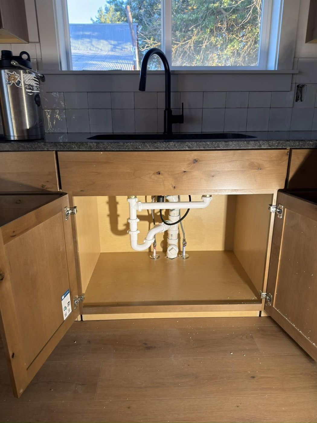 New kitchen sink and black faucet with clean under-sink plumbing